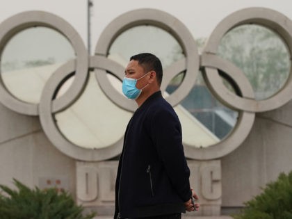 BEIJING, CHINA - MARCH 25: A Chinese man wears a protective mask as he walks past the Olympics rings at the Olympic park on March 25, 2020 in Beijing, China. The 2020 Tokyo Olympics have been postponed to no later than the summer of 2021 because of the coronavirus (COVID-19) …