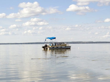horizontal image of a pontoon boat coasting on a beautiful blue lake under clear blue sky in the summer time.