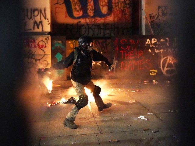 PORTLAND, OREGON - JULY 22: A protester throws flaming trash toward the Mark O. Hatfield U.S. Courthouse after breaking through a newly-reinforced perimeter fence on July 22, 2020 in Portland, Oregon. The night marked 56 days of protests in Portland following the death of George Floyd in police custody. (Photo …