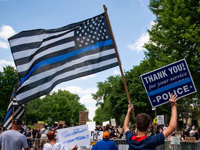 ST PAUL, MN - JUNE 27: A demonstrator holds a "Thin Blue Line" flag and a sign in support of police during a protest outside the Governors Mansion on June 27, 2020 in St Paul, Minnesota. A group called "Bikers for 45" advocating a pro-police stance arranged the protest and …