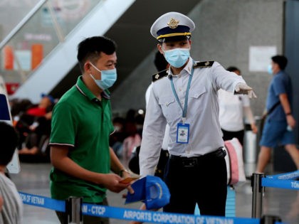 A staff member (R) from Vietnam's Centre of Disease Control assists passengers wearing face masks as they queue up for temperature checks at the departures terminal at Danang's international airport on July 27, 2020. (Photo by Hoang Khanh / AFP) (Photo by HOANG KHANH/AFP via Getty Images)