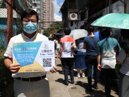 This photo taken on July 11, 2020 shows a volunteer (L) holding up a sign as people (R) queue to vote for New Territory East candidates during a primary election in Hong Kong. - China on July 14, 2020 has described a primary by Hong Kong's pro-democracy parties as a …