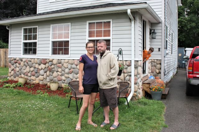 Crystal and Chris Martin stand outside their home, Sunday, July 19, 2020 in Burton, Mich., as one of their children looks on. The Martins, who had to defer some mortgage payments, are among millions of Americans who have struggled financially during the coronavirus pandemic. Crystal has been laid off since …