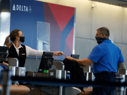 In this July 22, 2020 photo, a ticketing agent for Delta Airlines hands a boarding pass to a passenger as he checks in for a flight in the main terminal of Denver International Airport in Denver. .Air travel has collapsed because of the virus pandemic, and airlines are trying to …