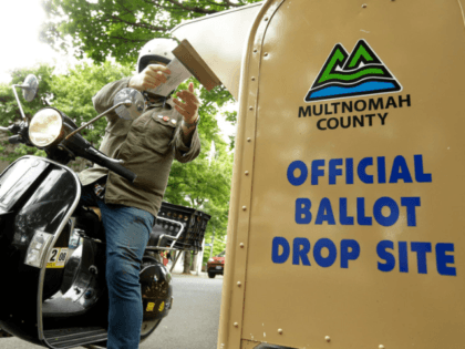 In this May 15, 2018, file photo, a voter drops off his ballot on the day of Oregon's primary election at a drive-by, drop-off station in Portland, Ore. Running an election by mail is a major undertaking, involving the U.S. Postal Service, armies of volunteers and even librarians. But for …