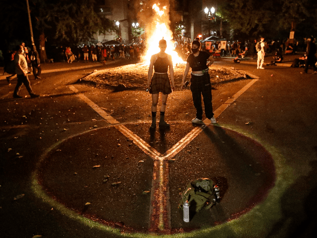 Demonstrators draw a peace sign in front of a fire during a Black Lives Matter protest at the Mark O. Hatfield United States Courthouse Tuesday, July 28, 2020, in Portland, Ore. (AP Photo/Marcio Jose Sanchez)