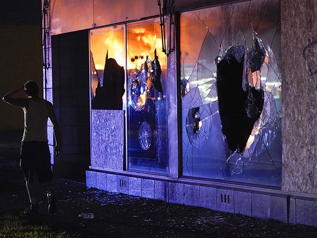 A protester walks past a building with broken windows as others burn during protests, Monday, Aug. 24, 2020, in Kenosha, Wis., sparked by the shooting of Jacob Blake by a Kenosha Police officer a day earlier. (AP Photo/Morry Gash)