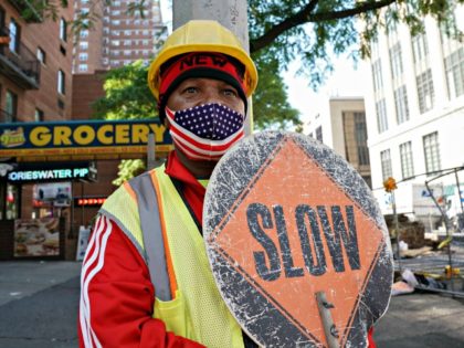 A man wearing an American flag mask directs traffic at a construction site in Chelsea on August 17, 2020 in New York. - Since the start official restart of construction in New York City workers have access to increased worksite hygiene as well as enhanced health screening requirements. (Photo by …