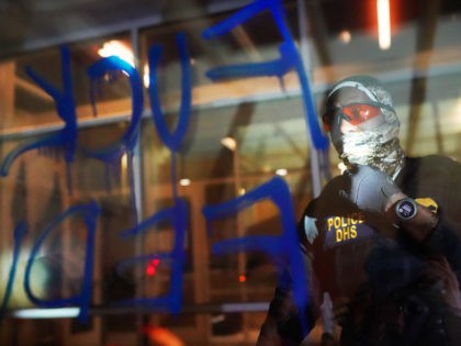A federal officers reads the words Fuck Feds written in graffiti on the front of the Immigration and Customs Enforcement (ICE) detention facility early in the morning on August 21, 2020 in Portland, Oregon. For the second night in a row federal police clashed with crowds in South Waterfront after …