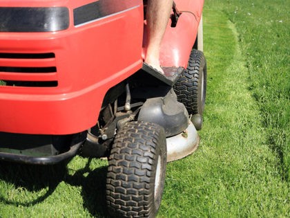 Red riding lawn mower (lawnmower, ride-on mower) in garden. Part of grass is mowed, piece