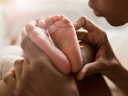 Close up portrait of African-American woman holding tiny feet of cute baby in sunlight, co