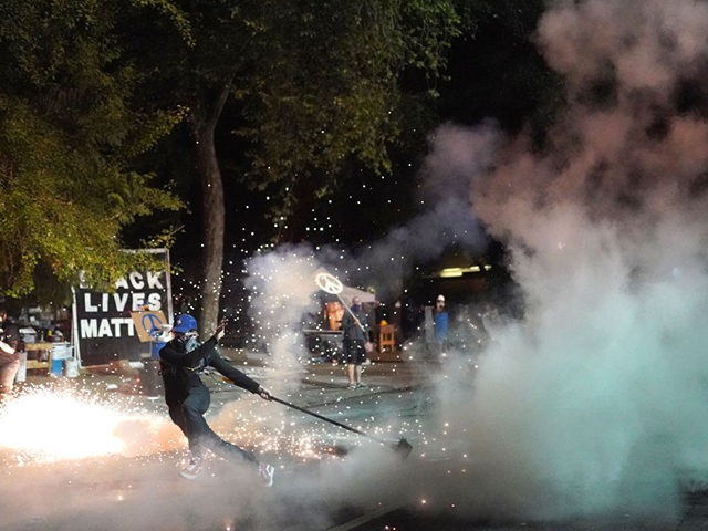 PORTLAND, OR - JULY 30: A protester flees as a flashing grenade explodes behind him during