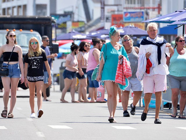 People, few wearing facemasks, walk on the boardwalk at Hampton Beach in Hampton, New Hampshire on August 5, 2020, as COVID-19 cases in New England are on the rise. - Hampton Beach is close to the boarder of Massachusetts and attracts thousands of people from Massachusetts every week to the …