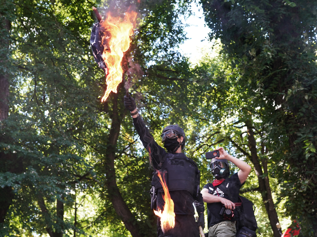 Anti-police protesters burn an American flag while facing off with right wing groups in front of the Multnomah County Justice Center on August 22, 2020 in Portland, Oregon. For the second Saturday in a row, right wing groups gathered in downtown Portland, sparking counter protests and violence. (Photo by Nathan …