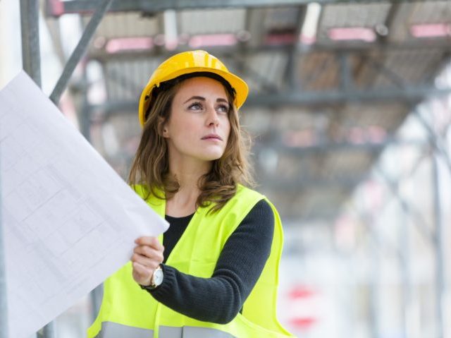 Female construction worker with helmet and safety jacket on construction site examining of