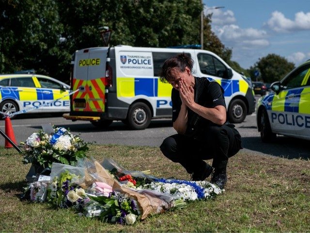 READING, ENGLAND - AUGUST 21: A police officer reacts as she looks at floral tributes left