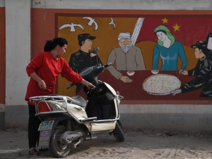 This photo taken on June 2, 2019 shows a Uighur woman beside a propaganda painting showing