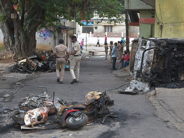 Policemen walk past burnt vehicles in Bangalore on August 12, 2020, after violence broke o