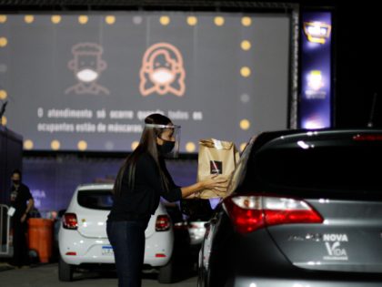 NITEROI, BRAZIL - JUNE 25: An employee delivers food to a moviegoer through the car window at a drive-in cinema at Caminho Niemeyer amidst the coronavirus (COVID-19) pandemic on June 25, 2020 in Niteroi, Brazil. The space has a capacity for up to 110 vehicles, and a 210 square meter …
