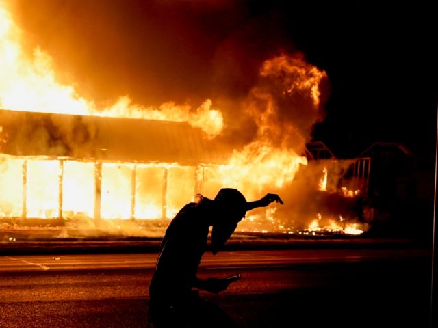 A protester walks past a building ablaze during protests Monday, Aug. 24, 2020, in Kenosha, Wis., sparked by the shooting of Jacob Blake by a Kenosha Police officer on Sunday. (AP Photo/Morry Gash)