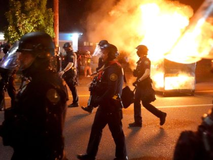 PORTLAND, OR - AUGUST 14: Portland police walk past a dumpster fire during a crowd dispers