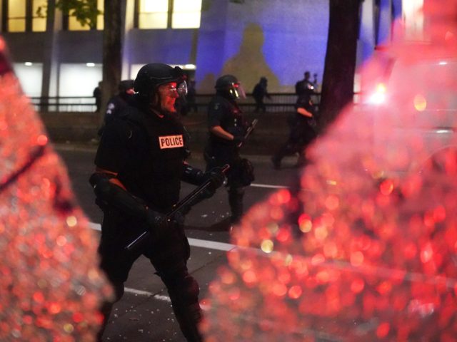 PORTLAND, OR - AUGUST 25: Portland police walk past the shattered glass of a bus stop while dispersing a crowd of about 150 people from Portland City Hall on August 25, 2020 in Portland, Oregon. Crowds chanted in support of Kenosha Wisconsin on the 90th night of protests Tuesday, where …