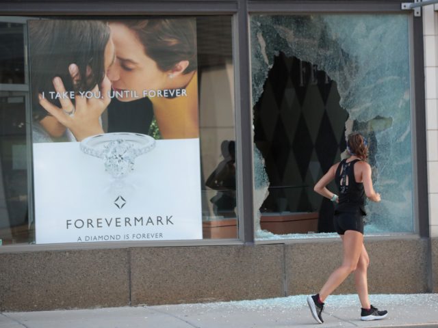 CHICAGO, ILLINOIS - AUGUST 10: A jogger runs past a broken storefront window after parts of the city had widespread looting and vandalism, on August 10, 2020 in Chicago, Illinois. Police made several arrests during the night of unrest and recovered at least one firearm. (Photo by Scott Olson/Getty Images)