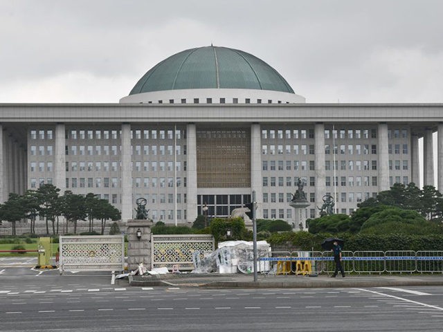 A police officer holding an umbrella stands guard in front of the National Assembly in Seo