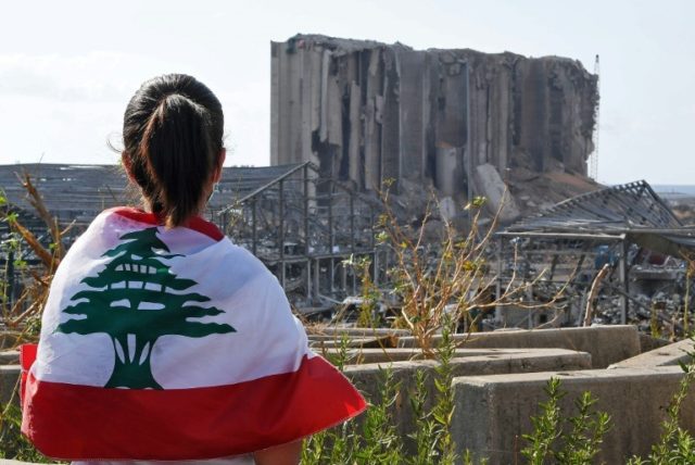 A Lebanese youth wrapped in the national flag looks at the damaged grain silos at Beirut's port, where a huge chemical explosion devastated large swathes of the capital © AFP -