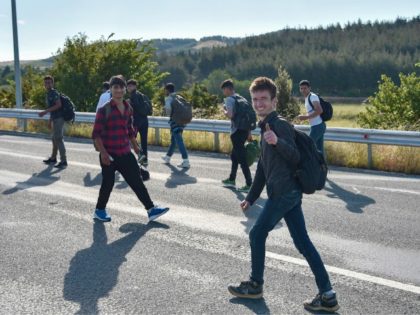 A migrant smiles and thumbs up as he walks with others on a road near Idomeni near the bor