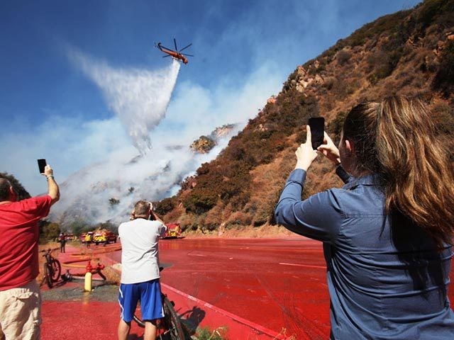 LOS ANGELES, CALIFORNIA - OCTOBER 21: Onlookers take photos as a firefighting helicopter m