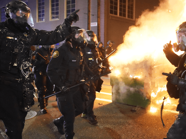 Portland police officers push protesters past a dumpster fire during a dispersal from in front of the Immigration and Customs Enforcement (ICE) detention facility in the early morning on August 21, 2020 in Portland, Oregon. For the second night in a row city police and federal officers clashed with protesters …