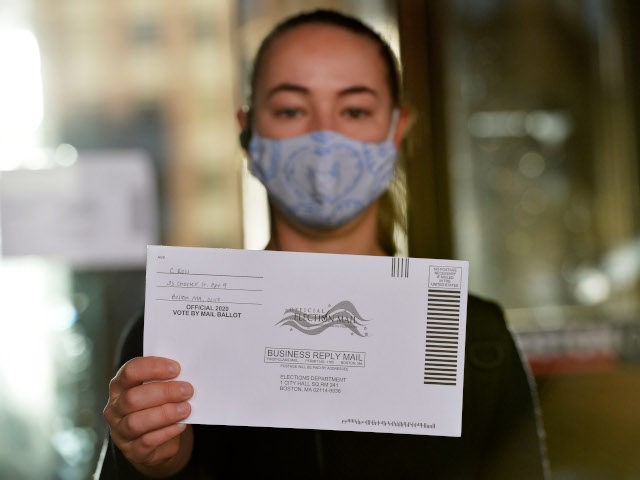 A woman holds up a mail-in ballot before dropping it off at Boston City Hall during the Ma