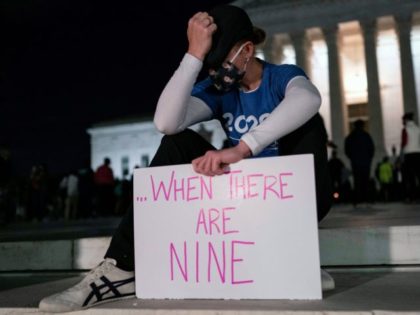 A woman holds a sign and gestures as people gather at a makeshift memorial for late Justic