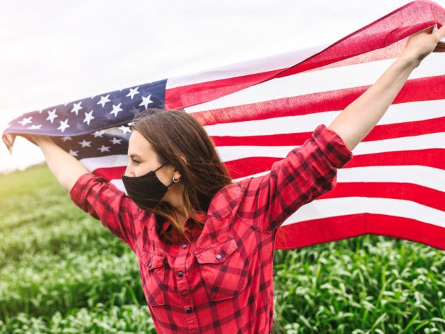 US flag is flying in hands of young woman in protective mask on her face