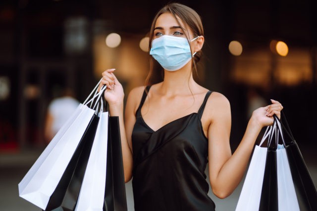 Young woman in protective sterile medical mask on her face with shopping bags enjoying in shopping.