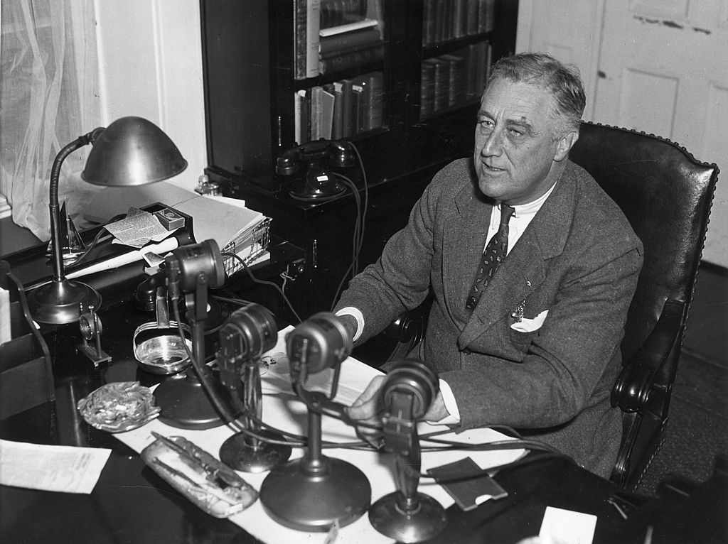 circa 1935: US president Franklin Delano Roosevelt (1882-1945) speaks into four radio microphones, which sit on his desk during one of his live nationwide 'fireside chat' broadcasts. (Photo by Hulton Archive/Getty Images)