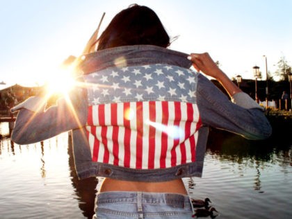 Close up of a girls fashionable jean American Flag jacket in front of a sunset. You can see a pond with ducks in the suburb background.