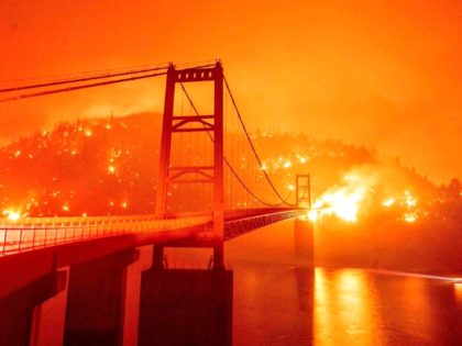 TOPSHOT - A boat motors by as the Bidwell Bar Bridge is surrounded by fire in Lake Oroville during the Bear fire in Oroville, California on September 9, 2020. - Dangerous dry winds whipped up California's record-breaking wildfires and ignited new blazes Tuesday, as hundreds were evacuated by helicopter and …