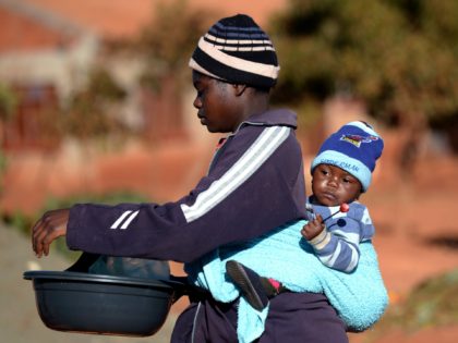 A woman carries her baby on her back as she shops at a market in Domboshava, 60km north of Harare, on August 1, 2013. Vote counting is under way on August 1 after Zimbabwe's tightly fought election which regional observers said was "orderly and fair" despite charges of vote-rigging by …