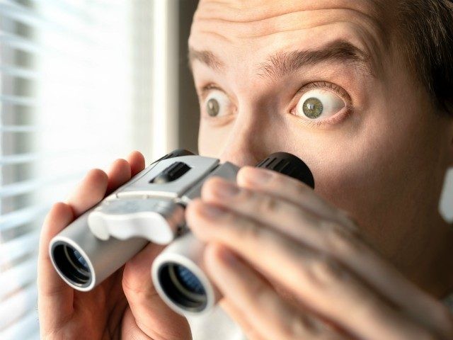 Surprised man with binoculars. Curious guy with big eyes. Nosy neighbour stalking or snooping secrets, gossip and rumour. Silly funny face. Shocked about unbelievable news. - stock photo