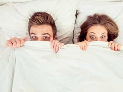 Surprised funny couple in love lying on bed under blanket - stock photo Surprised funny co