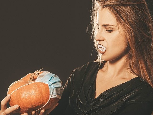 Halloween holiday concept during quarantine - vampire with pumpkin and medicinal mask