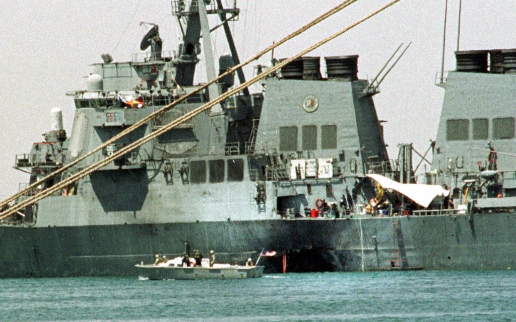 A small boat guards the USS Cole in Aden, Yemen Friday Oct. 20 2000. Investigators have found bomb-making equipment in an apartment near the Yemeni port and believe two former occupants may have carried out the suicide bomboing that killed 17 sailors aboard the USS Cole. (AP Photo/Hasan Jamali)