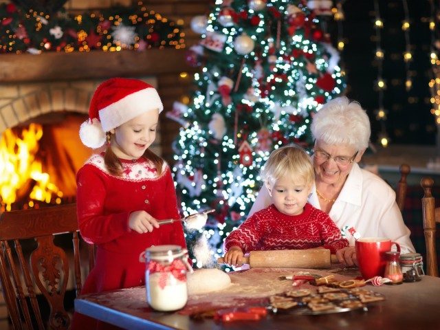 Grandmother and children baking Christmas cookies at fire place and Xmas tree. Kids and gr