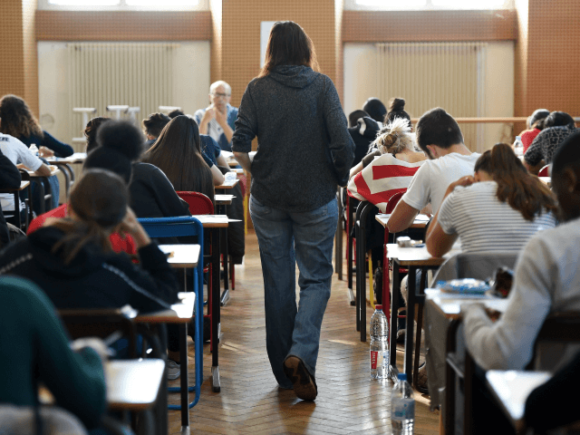 A teacher walks through a classroom as high school students take the philosophy exam, the first test session of the 2019 baccalaureate (high school graduation exam) on June 17, 2019 at the Pasteur high school in Strasbourg, eastern France. (Photo by FREDERICK FLORIN / AFP) (Photo credit should read FREDERICK …