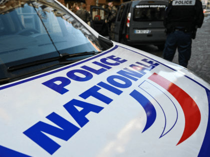 A French police officer stands next to a French "Police Nationale" car as soldie