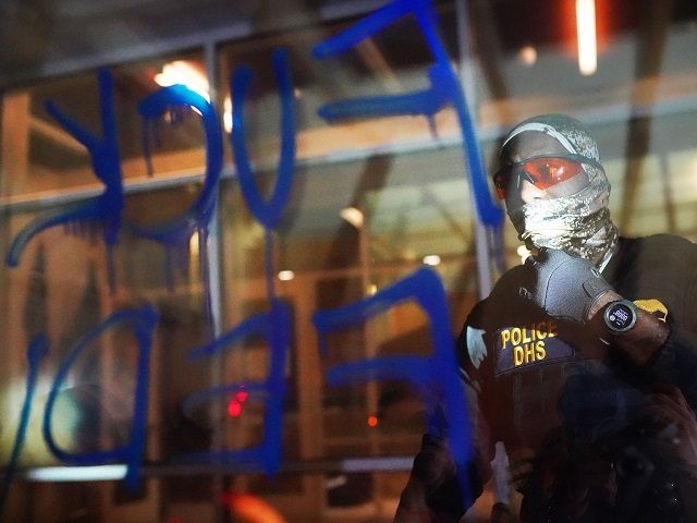 PORTLAND, OR - AUGUST 21: A federal officers reads the words Fuck Feds written in graffiti on the front of the Immigration and Customs Enforcement (ICE) detention facility early in the morning on August 21, 2020 in Portland, Oregon. For the second night in a row federal police clashed with …