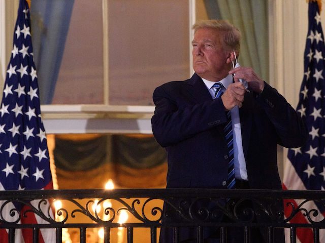 US President Donald Trump takes off his facemask as he arrives at the White House upon his