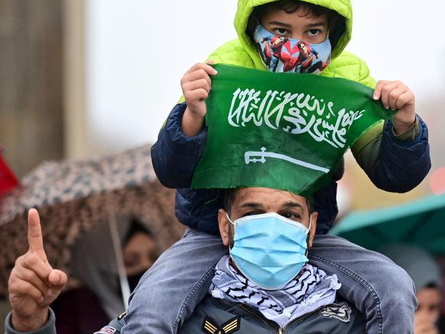 A young demonstrator holds the national flag of Saudi Arabia featuring the Islamic creed d